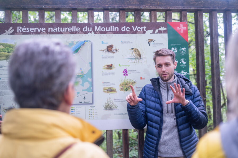 Un homme fait une présentation en langue des signe devant un panneau de la Réserve naturelle du Moulin de Vert, à Cartigny