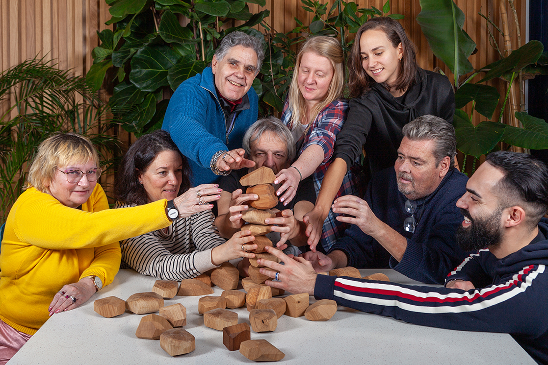 Plusieurs personnes souriantes essaient de faire tenir des bouts de bois en équilibre