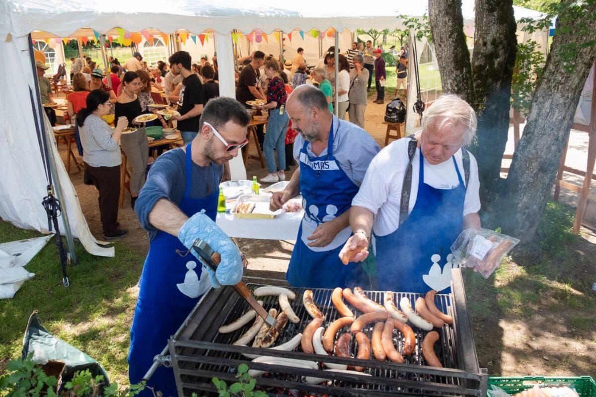 Grillade de saucisse lors d'un évènement, avec de nombreuses personnes en arrière plan sous une grande tente