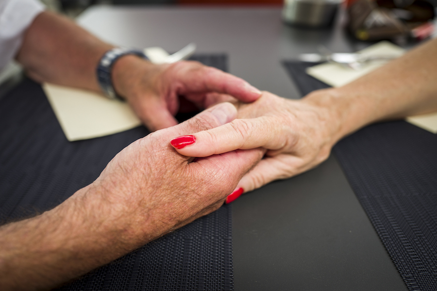 Une mains avec du vernis à ongle rouge est posée sur la main d'une autre personne.