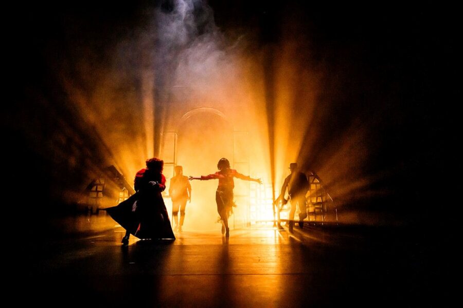 Une lumière provenant du fond de la scène éclaire quatre comédiens. Cet effet, à contre-jour, et celui d'un épais brouillard nous laissent deviner leurs silhouettes ainsi qu'une arche qu’ils franchissent. Photo de Lauren Pasche.