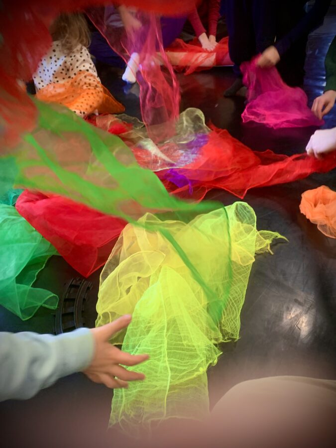 Des mains d'enfants tiennent des foulards de toutes les couleurs pour former au centre de l'image un bel ensemble coloré dans un joyeux désordre recherché.
